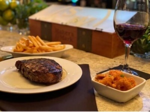 image of buttery ribeye steak with side dish of french fries and fried shrimp with a glass of red wine at The SteaKhouse in Hammond La